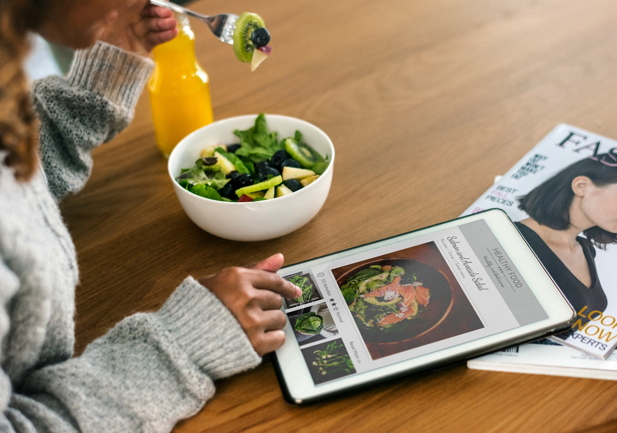 Person eating a fresh salad while reading on a tablet — Virgo-Meds patient resources